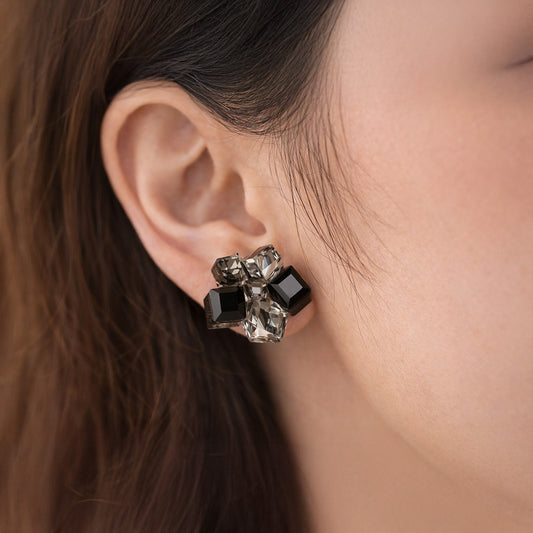 Close-up of an ear wearing a decorative earring with black and clear gemstones.