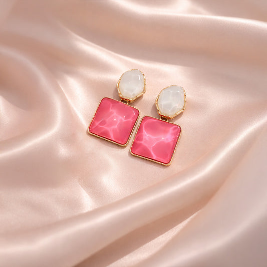 Pink square earrings with gold accents on a pink satin background