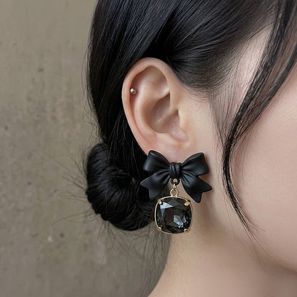 Black bow earring with a dark gemstone on an ear against a neutral background