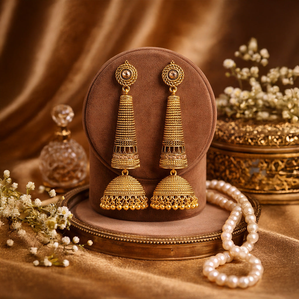 Traditional gold jhumka earrings with intricate design placed on luxury velvet stand with pearls and decorative props