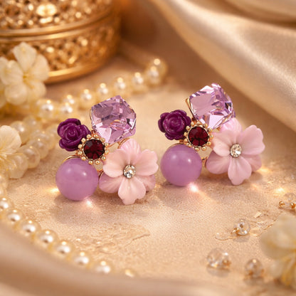 Pair of decorative earrings with flowers and gemstones on a gold surface.